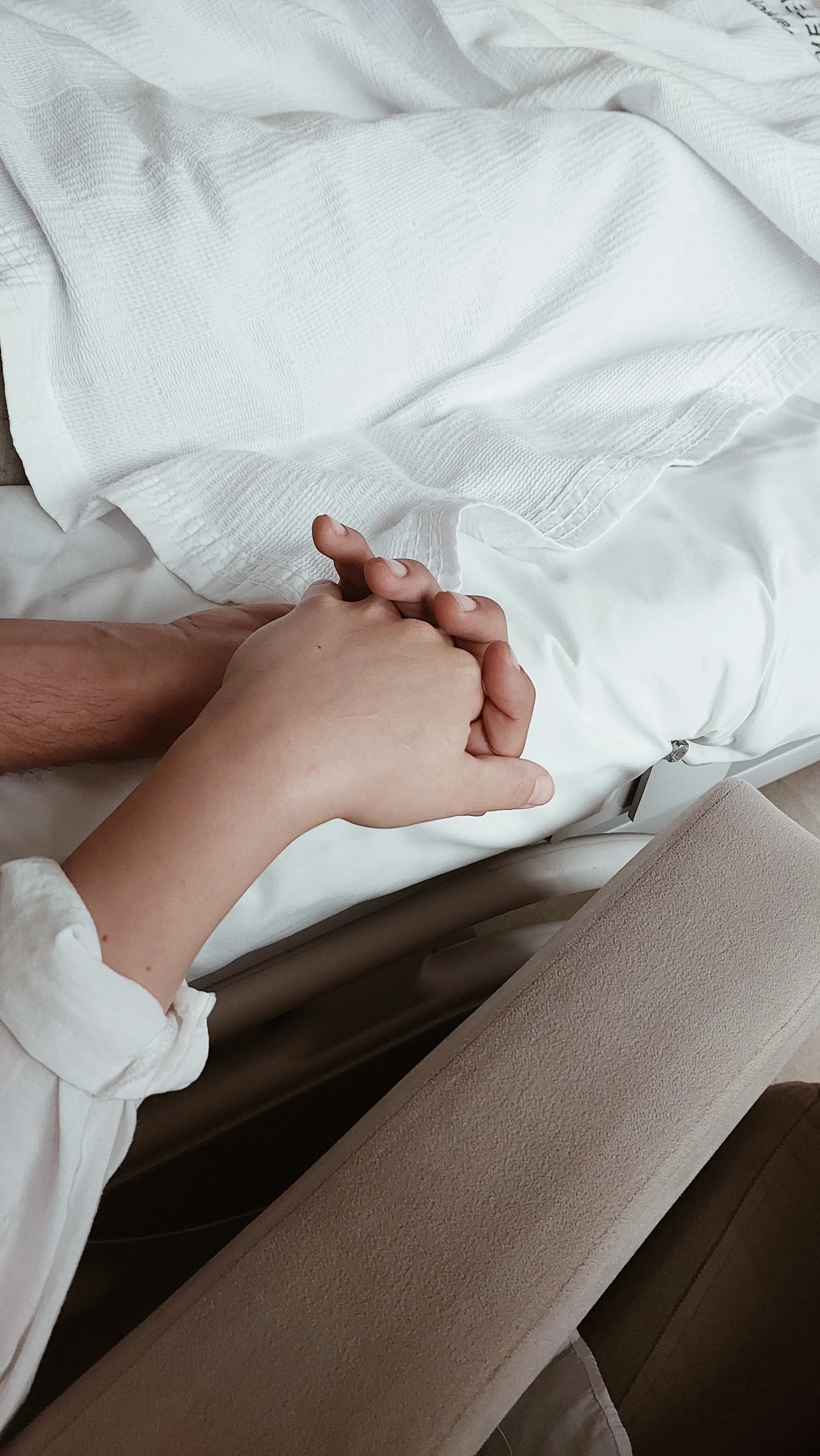 Close-up of hands reaching for one another on bed linen