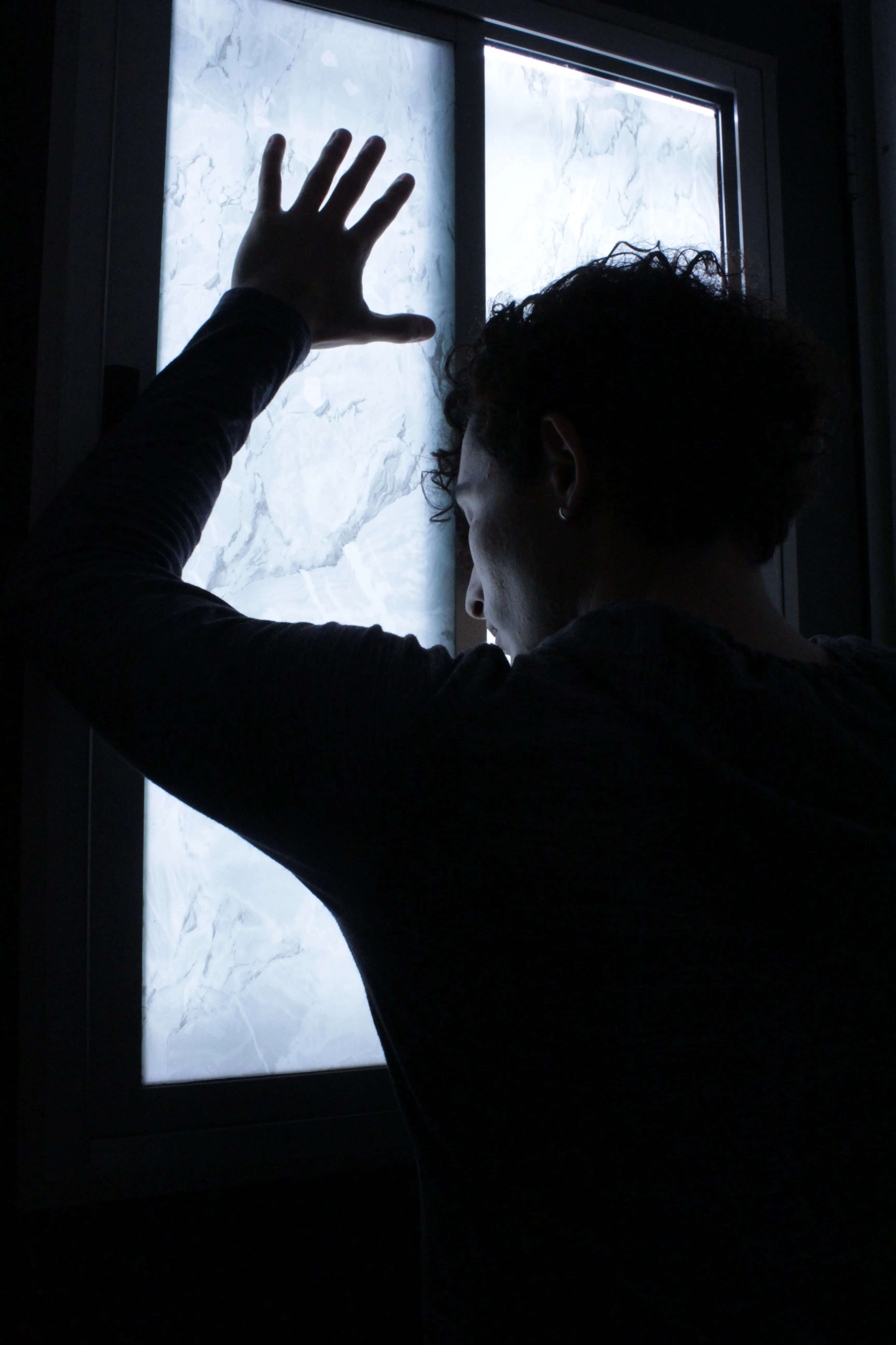 Anonymous figure silhouetted at a window in quiet reflection