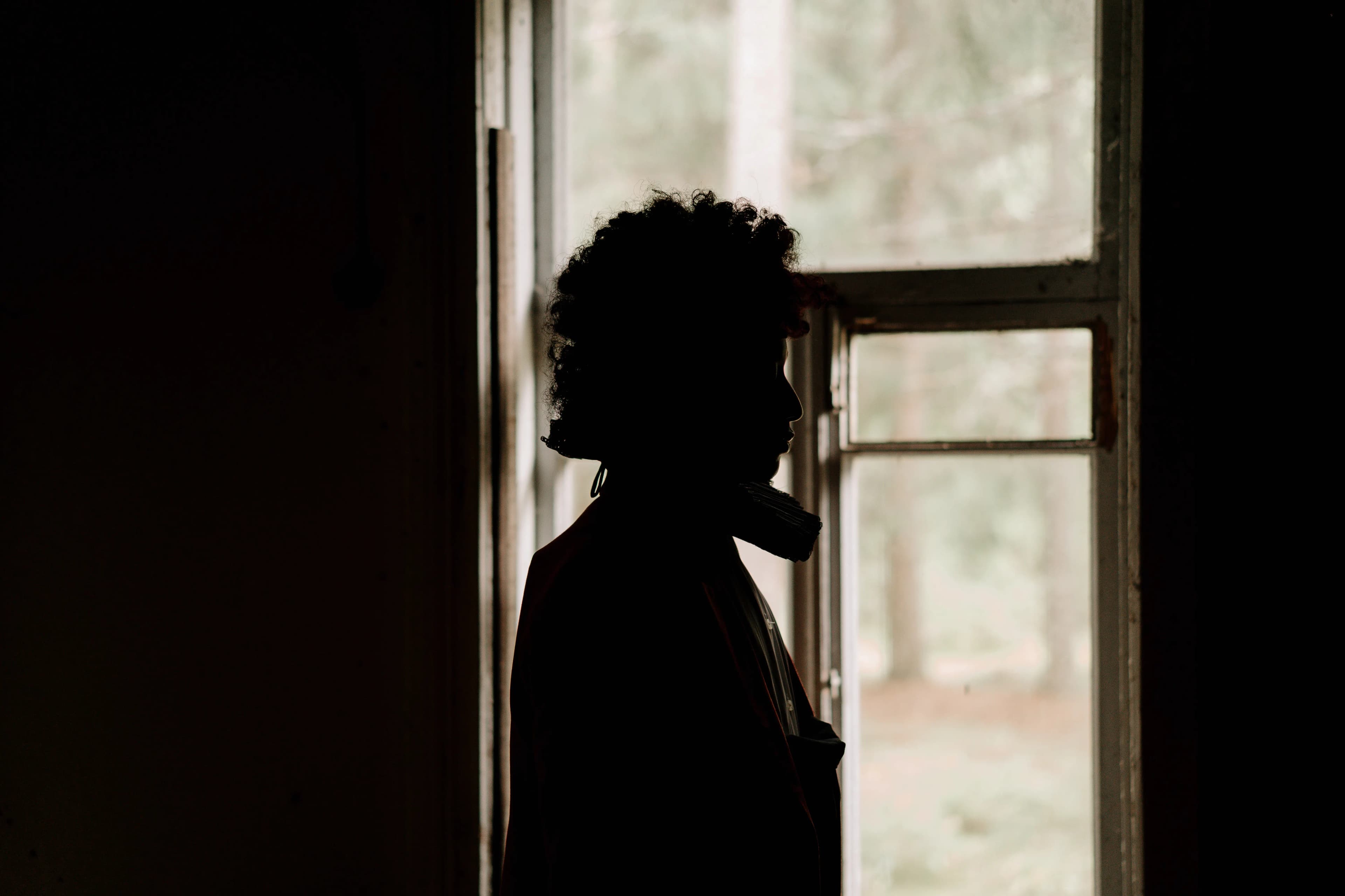 Person standing thoughtfully by an open window in soft light