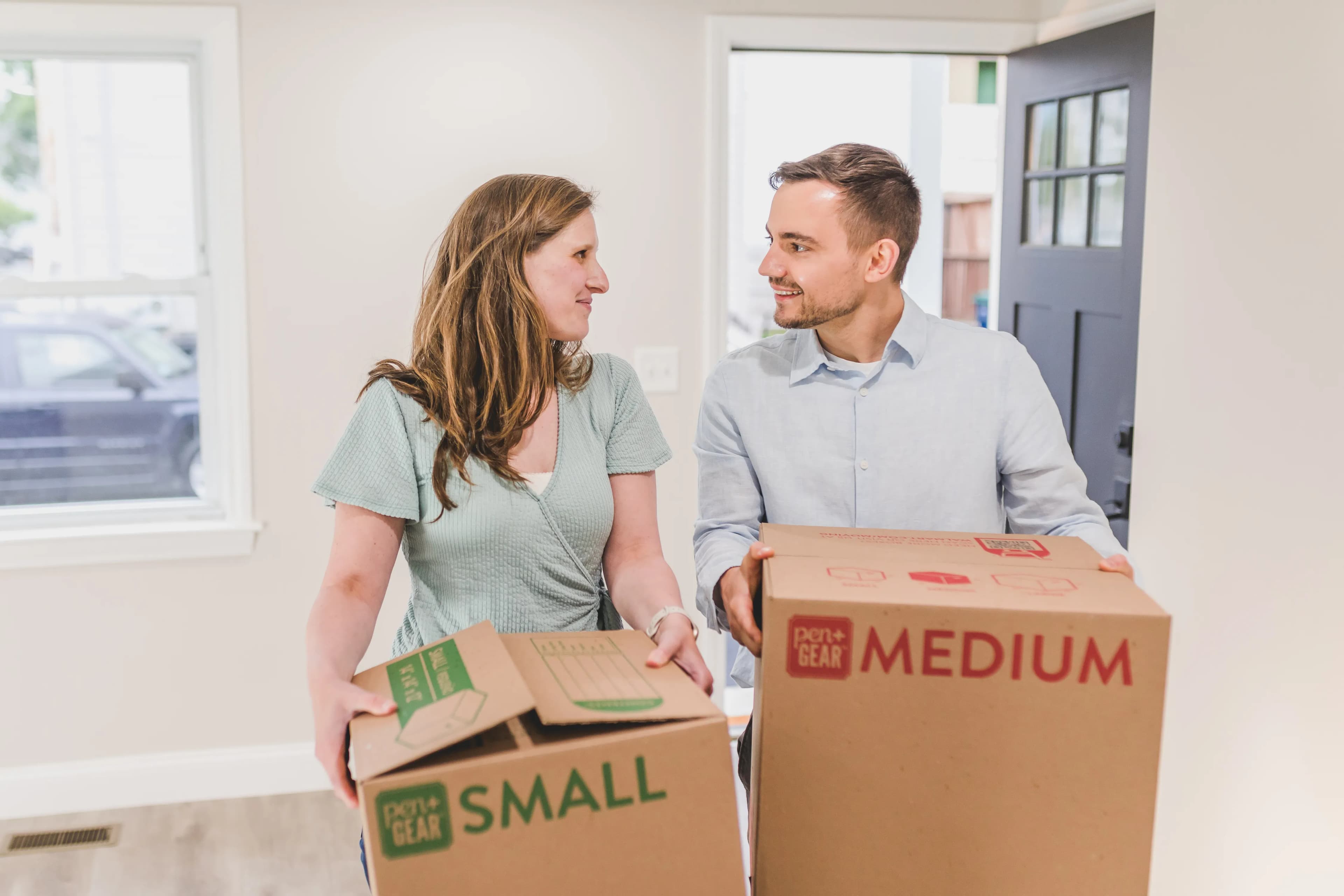 Two people carrying boxes into a new living room