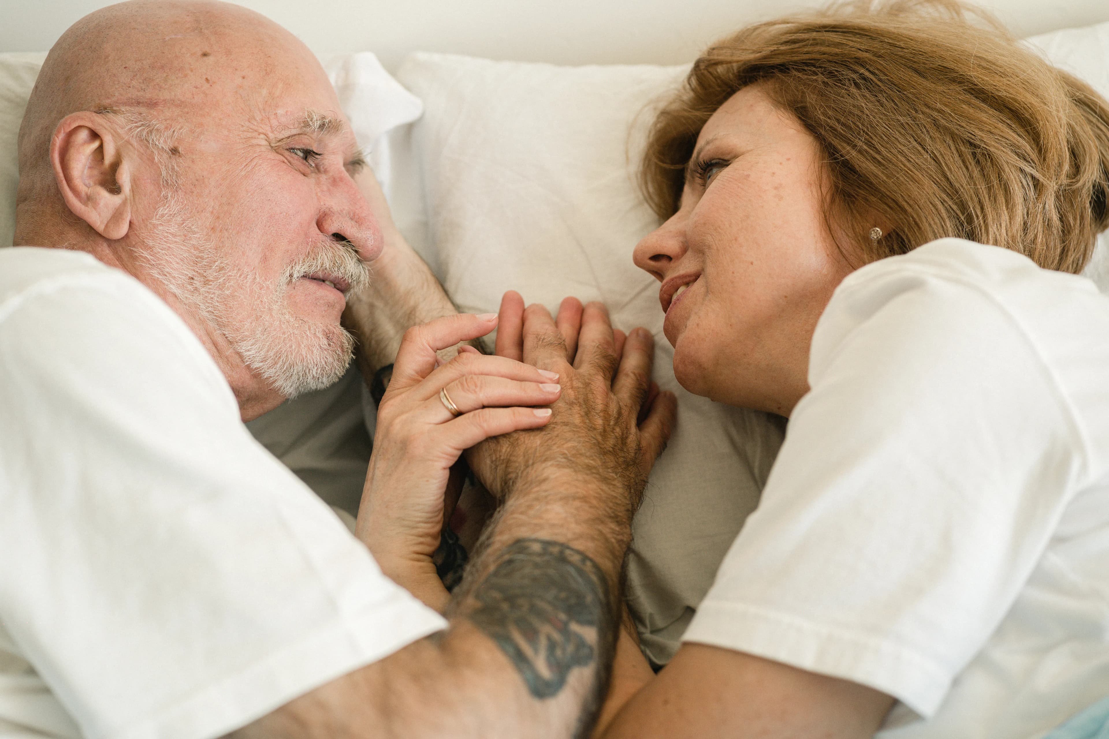 Older couple smiling and holding hands while lying in bed