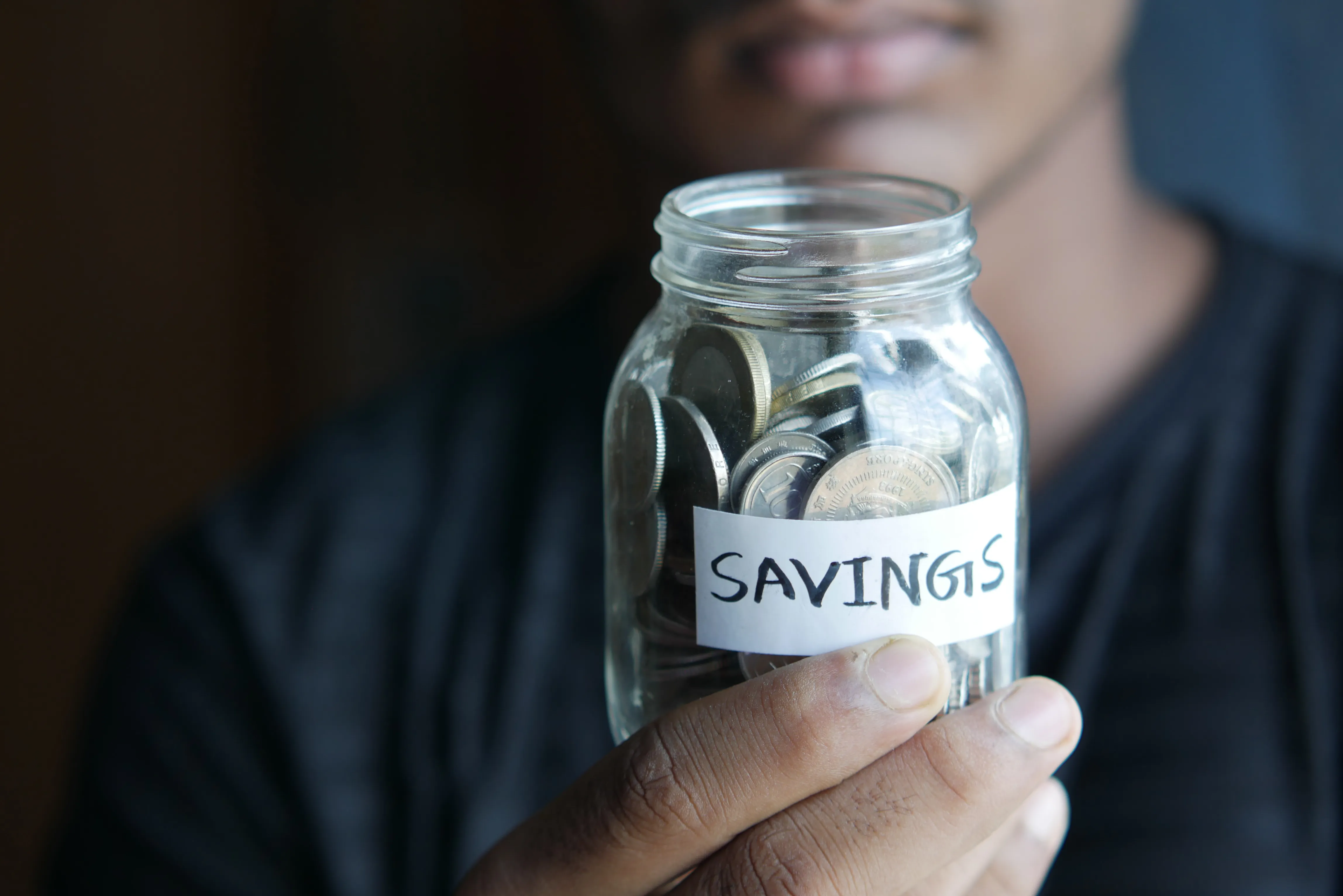 Close-up of a hand holding a jar of savings coins