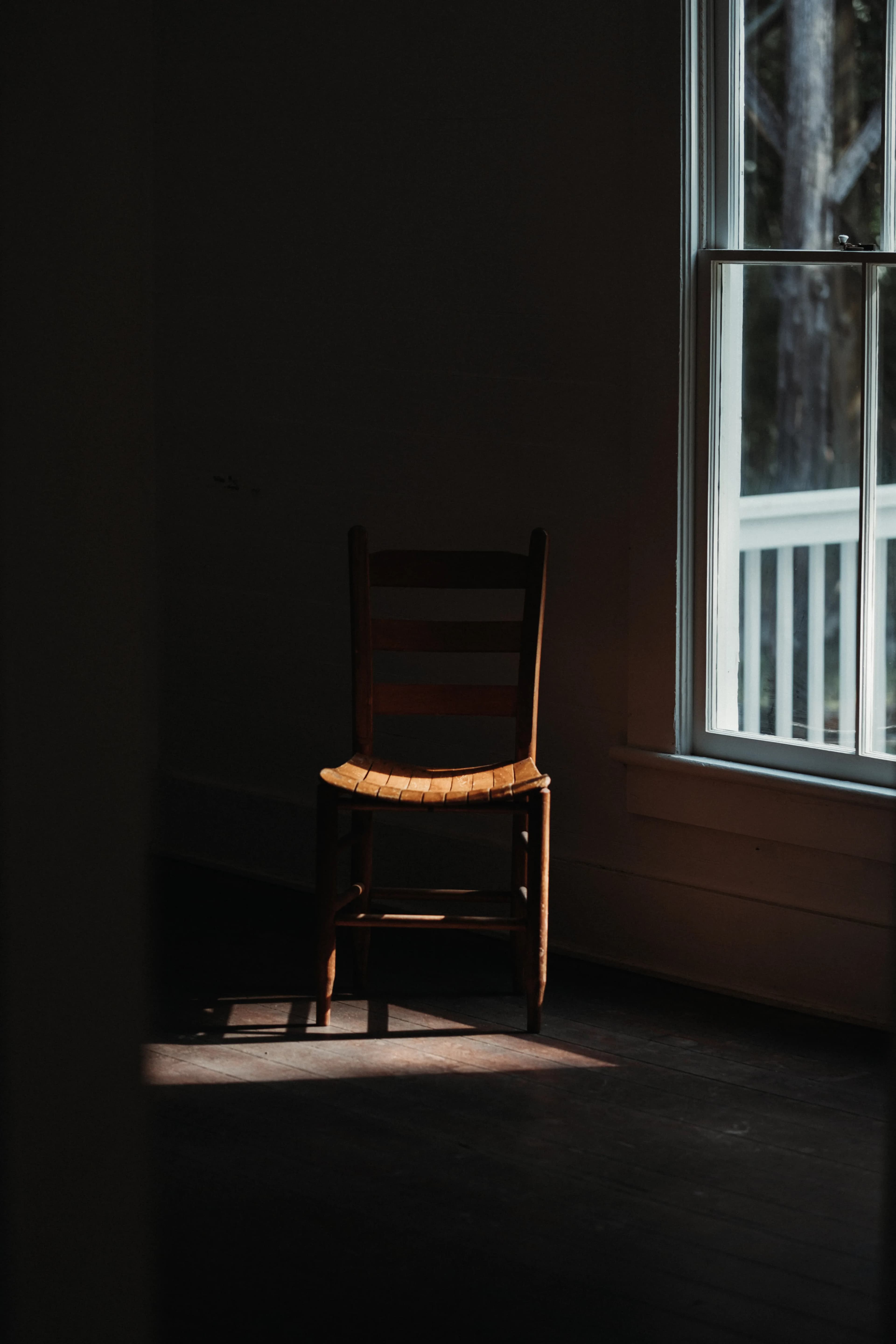 Empty wooden chair by a window in a sunlit room