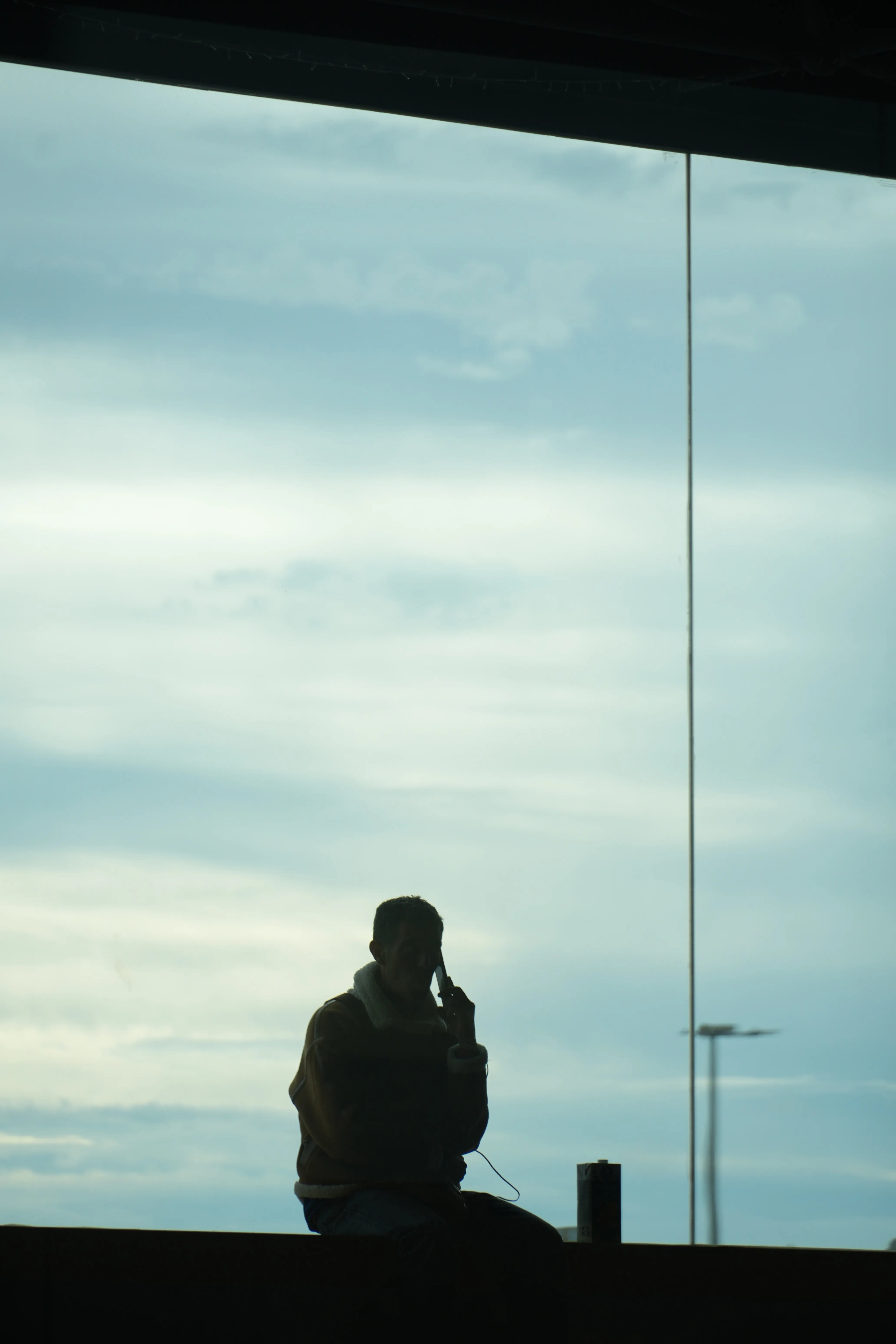 Person sitting alone beside a large window in quiet reflection