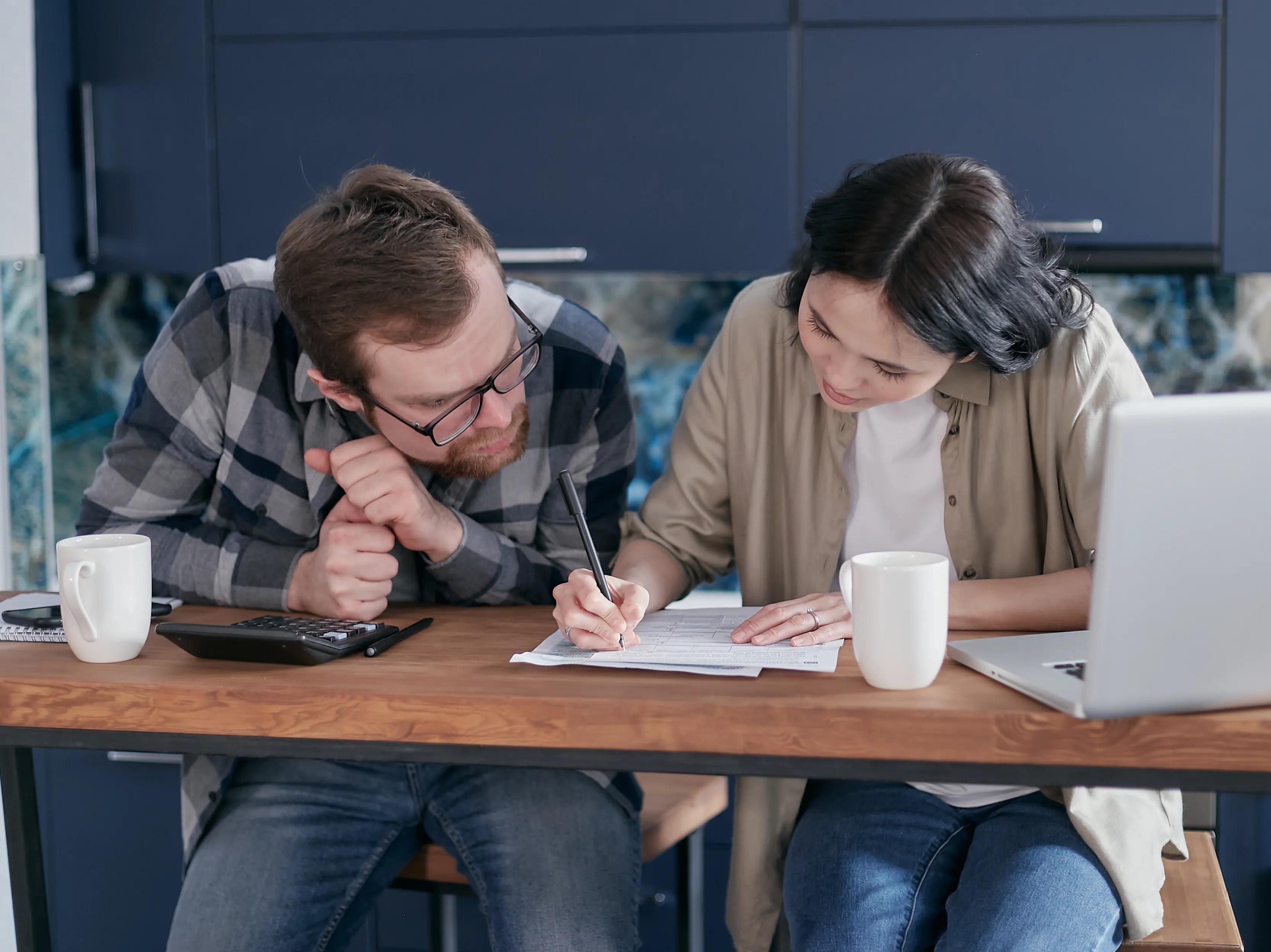 Two partners reviewing detailed paperwork at a kitchen table